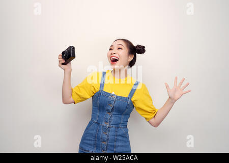 Überrascht, Frau, mit top knot Frisur, das Tragen von Jeans Overall, Holding retro Kamera, auf dem weißen Hintergrund Stockfoto