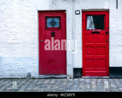 Zwei rote Holz Haustüren in die weiße Wand. Zwei vintage rot Türen mit Fenster am oberen. Stockfoto