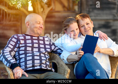 Glückliche Großeltern ihre Enkel draußen genießen. Family Portrait. Schöne glückliche Großmutter und Großvater, Enkelin Buch lesen in der Natur bei Sonnenuntergang. Stockfoto