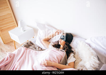 Dunkelhaarige schöne junge brunette schlafend in ihrem Bett. Schwarz Schlafbrille auf die Augen. Allein im Schlafzimmer. Träume Stockfoto