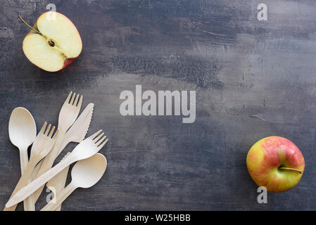 Blick von oben auf die verstreuten Gabeln, Messer und Löffel aus Holz - eco Besteck. Frischen Apfel Obst lag auf dem Hintergrund von Marmor Arbeitsplatte in der Küche. Kopieren Sie Platz für Stockfoto