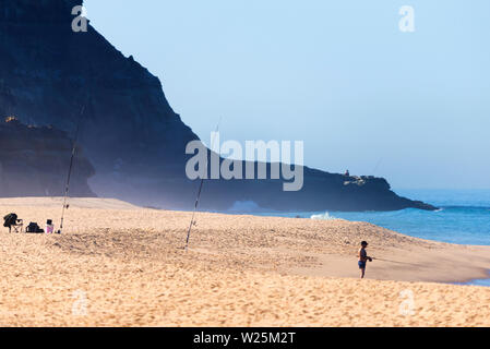 Allein Fischer mit Angeln am Strand versucht sein Glück, wie die Wellen auf den Sand am Meer Strand schoß. Stockfoto