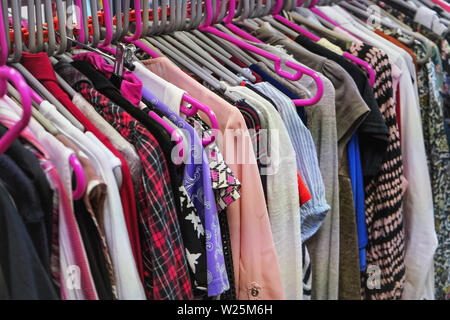 Verschiedene Frauen Kleidung auf meist rosa Kleiderbügel in Liebe second hand Thrift Shop Stockfoto