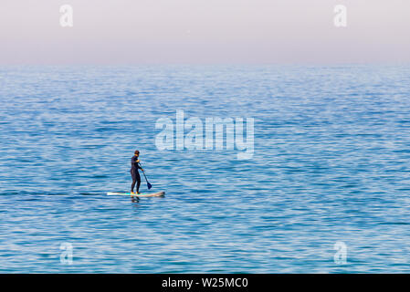 Stand Up Paddle Boarder im Neoprenanzug paddeln auf einem See. Minimalistisches Bild. Stockfoto
