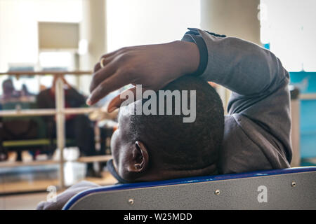 Müde anonyme afrikanischen Mann in Flughafen Halle, Ansicht von hinter Detail auf der Hand über seinen Kopf warten Stockfoto