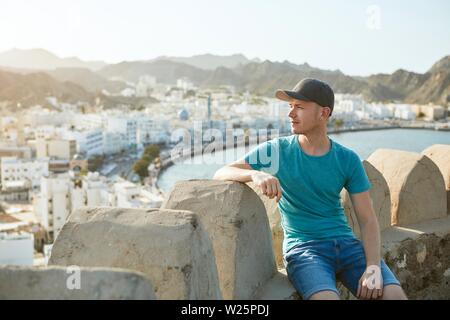 Reisende in Muscat. Junger Mann gegen alte Stadt, Meer und Gebirge in Oman. Stockfoto