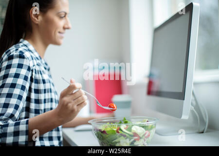 Mitarbeiterin im Büro in gesunden Salat Mittagessen am Schreibtisch Stockfoto