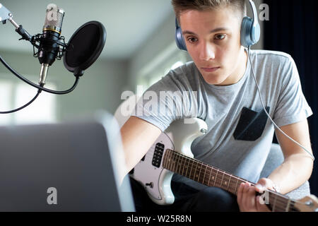 Teenager Gitarre Spielen und Aufnehmen von Musik auf Laptop zu Hause Stockfoto