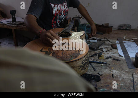 GIANYAR, Bali/Indonesien - 30. MAI 2019: Eine klassische Gitarre Handwerker ist die Paarung Gitarre Saiten seiner Gitarre. Er paßte auch die Gitarre Ton am Git Stockfoto