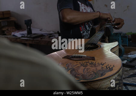 GIANYAR, Bali/Indonesien - 30. MAI 2019: Eine klassische Gitarre Handwerker ist die Paarung Gitarre Saiten seiner Gitarre. Er paßte auch die Gitarre Ton am Git Stockfoto