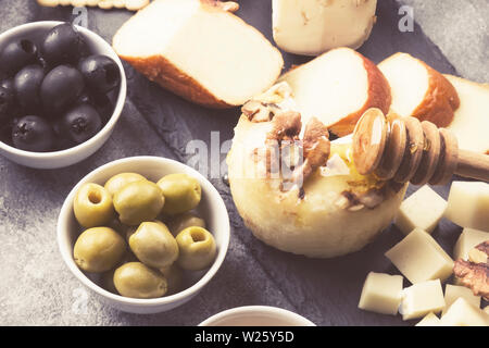 Snacks mit Wein - verschiedene Arten von Käse, Feigen, Nüsse auf grauem Hintergrund. Getönt Stockfoto