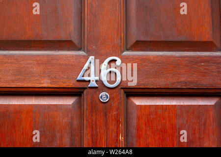 Haus Nummer 46 bei den sechsundvierzig in Metall Ziffern auf einem natürlichen roten gemasertem Holz- Vordertür Stockfoto