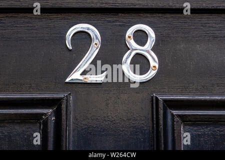 Haus Nummer 28 mit der Achtundzwanzig in glänzendem Silber metall Ziffern auf schwarzem Holz vordere Klappe Stockfoto