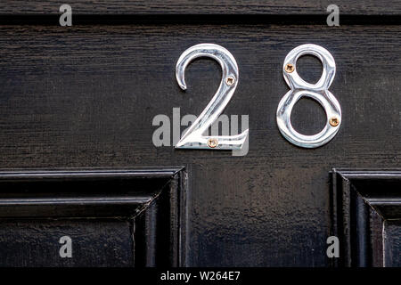 Haus Nummer 28 mit der Achtundzwanzig in glänzendem Silber metall Ziffern auf schwarzem Holz vordere Klappe Stockfoto