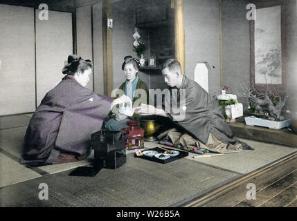 [1900s Japan - Japanische Neues Jahr - Trinken Willen] - eine Frau, gießt ein enger Freund der Familie einige Toso, einem besonderen Willen, während das neue Jahr feiern. Dieses Bild ist Teil des neuen Jahres in Japan, ein Buch von Kobe veröffentlicht Fotograf Kozaburo Tamamura 1906 (Meiji 39). 20. Jahrhundert vintage Lichtdruck drucken. Stockfoto