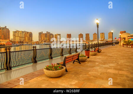 Bänke an der Marina corniche Gehweg in Porto Arabien am Pearl-Qatar, Doha, mit Wohn- Hochhäuser der künstlichen Insel bei Nacht beleuchtet Stockfoto