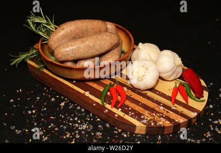 Frische Rohwürste in einer Schüssel auf einem Holzbrett Bereit zum Kochen Stockfoto