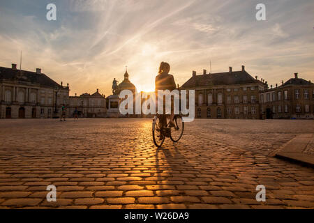 Ein hübsches Mädchen reitet ihr Fahrrad, wie die Sonne am Schloss Amalienborg, Kopenhagen, Dänemark, wie die Sonne Stockfoto