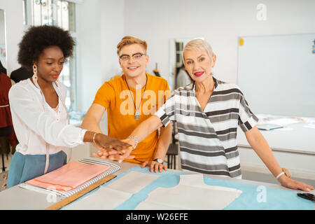 Hände zusammen. Drei moderne glücklich Modedesigner zeigen Teamgeist durch die Hände übereinander Stockfoto