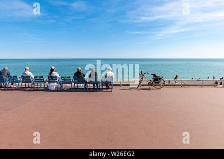 Menschen sitzen auf einer öffentlichen Bank und blicken auf das Mittelmeer an der Promenade des Anglais in Nizza, Südostfrankreich, Europa Stockfoto