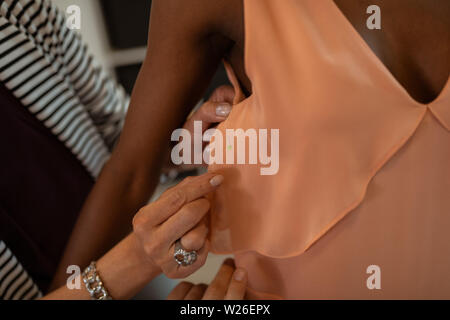 Stift auf ein Kleid. Nahaufnahme der weiblichen Mode Designer Hände einstellen orange Kleid ist ein Modell, das unter Verwendung von Pins Stockfoto
