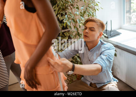 Bekleidung details. Blonde junge Modedesigner der Anbringung der neuen orange Kleid auf das Modell in einem Studio Stockfoto