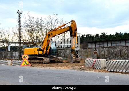 Bagger auf einer Baustelle im Verlauf der Verlegung von Abwasserleitungen und Kommunikation auf einer Straße in der Stadt Stockfoto