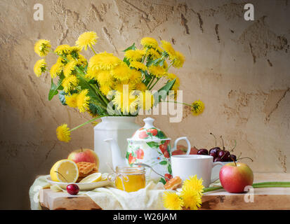 Stillleben mit Löwenzahn, Wasserkocher, Obst und Honig auf Holztisch auf alten Risse im Hintergrund. Stockfoto