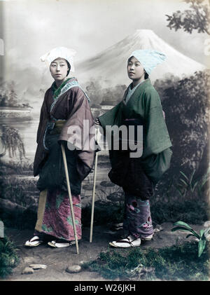 [1890s Japan - Japanische Frauen in Reisen Tragen] - Ein studio Foto von zwei Frauen gekleidet für Reisen. Halten Sie Stöcke und Tücher um den Kopf gewickelt. Ihre Kimonos werden bis zur leichteren Bewegung gebunden. 19 Vintage albumen Foto. Stockfoto