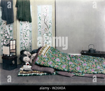 [1890s Japan - Japanische Frauen Schlafen] - Ein studio Foto von zwei Frauen in wattierte Futon Betten schlafen mit dem Kopf auf hölzernen Kopf unterstützt. Es muss im Winter sein, da sie zwei Schichten sowohl für die Matratze und Abdeckung verwenden. Es ist ein Ando Lampe in der Nähe von ihren Köpfen. Ein Paravent mit Blumen und Vögel illustriert steht dahinter. Die in der Nähe ihrer Füße ist ein hakohibachi (brazier in einer Holzkiste verpackt) mit einem tetsubin (Bügeleisen, Wasserkocher). 19 Vintage albumen Foto. Stockfoto
