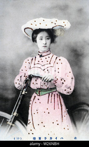[1900s Japan - Japanische Frau in westlicher Kleidung mit Fahrrad] - eine Frau wirft mit einem Fahrrad, das Tragen eines westlichen stil kleid und hut. 20. jahrhundert alte Ansichtskarte. Stockfoto