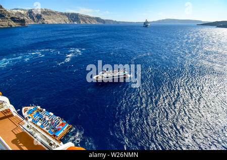 Ein Angebot Boot zieht neben einer massiven Kreuzfahrtschiff mit einem anderen Boot und Schiff in der Ferne in die Caldera von Santorin, Griechenland Stockfoto