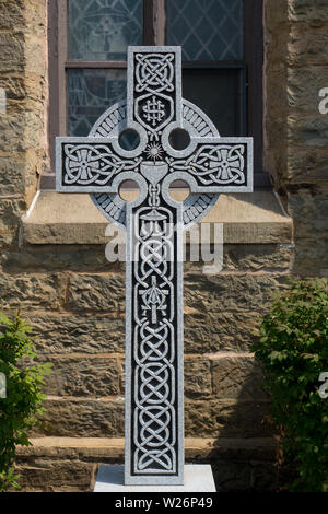 Eine reich verzierte Granit Celtic Cross aus dem Grab von einem römisch-katholischen Priester, die die keltischen Knoten Muster, einer Gemeinschaft, Kelch, und das IHS Symbol Stockfoto