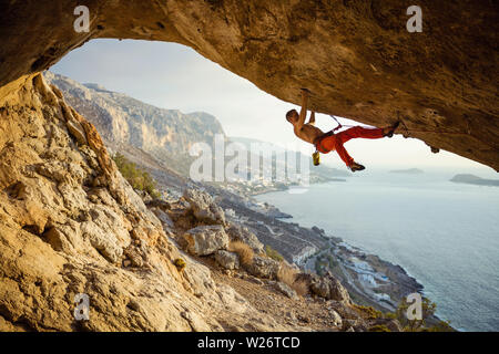 Kaukasischen jungen Mann klettern anspruchsvolle Strecke, die in der Höhle gegen die wunderschöne Aussicht der Küste Stockfoto