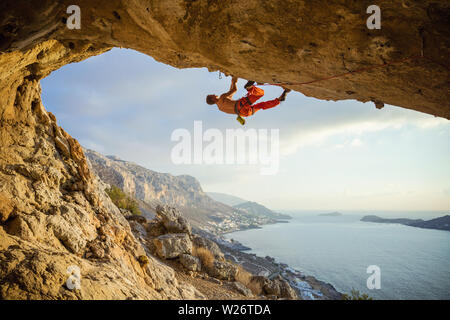 Kaukasischen jungen Mann klettern anspruchsvolle Strecke, die in der Höhle gegen die wunderschöne Aussicht der Küste Stockfoto