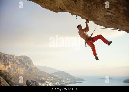 Junger Mann klettern anspruchsvolle Strecke, die in der Höhle gegen die wunderschöne Aussicht der Küste Stockfoto
