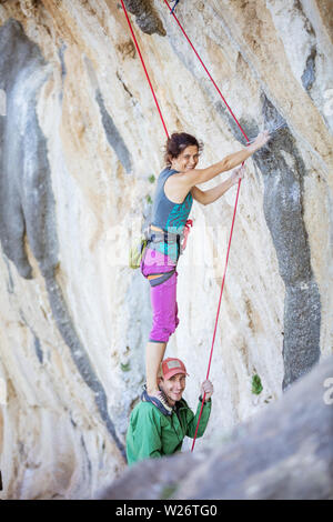 Freundliche weibliche Kletterer stehen auf den Schultern ihres Partners, um klettern anspruchsvolle Strecke Stockfoto