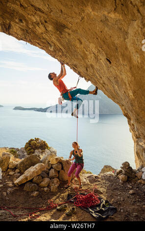 Junger Mann beginnt Klettern anspruchsvolle Strecke, die in der Höhle, seine Partnerin sichern ihm Stockfoto