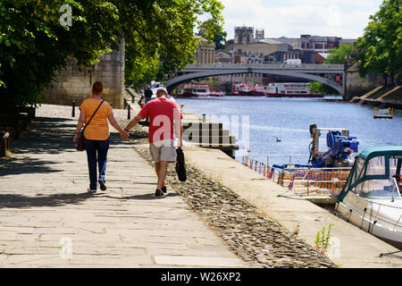 Beim Spaziergang am Fluss Ouse sind ein Mann und eine Frau Hand in Hand, Dame Judi Dench Walk, York, North Yorkshire, England, Großbritannien. Stockfoto