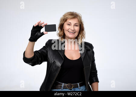 Gerne reife pensionierte Frau in Schwarz Jacke zeigt leere Kreditkarte. Aktiven Lebensstil im Alter. Stockfoto