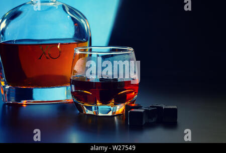 Wiederverwendbare Eiswürfel oder Schwarz shungite kühlen Bausteine mit Glas Malt Whisky und kleine Karaffe über einen dunkelblauen Hintergrund in einem Pub Stockfoto