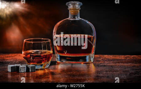 Flasche und Glas Brandy mit wiederverwendbaren Eiswürfel oder kühlen Blöcke auf eine rustikale Bar Theke mit smokey Atmosphäre und Raum kopieren Stockfoto