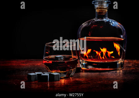 Flasche Cognac oder Whisky, was einem die Fames ein warmes Feuer im Winter mit einem Glas sprits und Schwarz wiederverwendbare Eiswürfel oder kühlen Eiswürfel Stockfoto