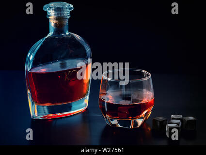 Flasche Cognac oder Whisky mit vollem Glas und schwarzem kühlen Eiswürfel oder wiederverwendbare Eiswürfel auf einem dunklen Hintergrund mit Kopie Raum Stockfoto