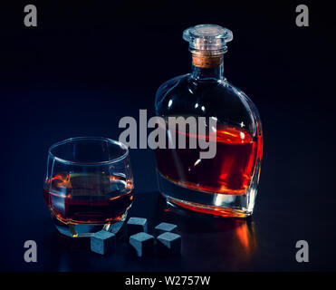 Schwarz shungite kühlen Eiswürfel mit einem Glas Whiskey und kleinen verschlossenen Dekanter auf einem dunklen Hintergrund konzeptionelle Nachtleben Stockfoto