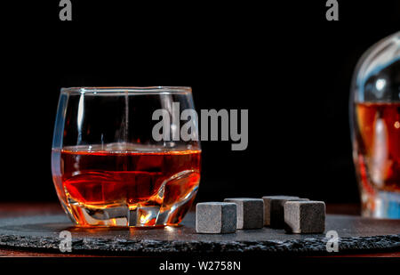 Glas Whiskey mit schwarzen kühlen Eiswürfel oder wiederverwendbare Eisblöcke gesehen niedrigen Winkel auf einem Bartresen mit Kopie Speicherplatz auf einem dunklen Hintergrund Stockfoto