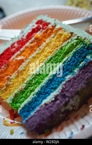 Nahaufnahme einer Scheibe einer rainbow Geburtstag Kuchen auf eine Platte. Hochformat. Stockfoto