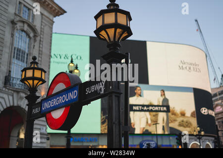 London, UK - Juni, 2019. Eine U-Bahnstation Eingang anmelden Piccadilly Circus, mit der berühmten Werbetafeln auf dem Hintergrund. Stockfoto