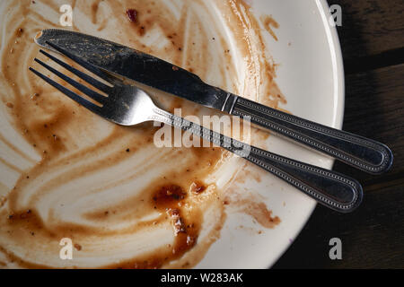 Eine Schmutzig weiße Schale mit Sonntagsbraten Soße übrig gebliebene und Besteck. Querformat. Stockfoto