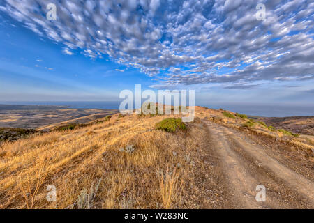 Rocky Road, über Hügel, durch mediterrane Landschaft auf der Insel Zypern mit Blick auf das Meer im Hintergrund. Die heiße semi-ariden Klima hat die BSh corr Stockfoto